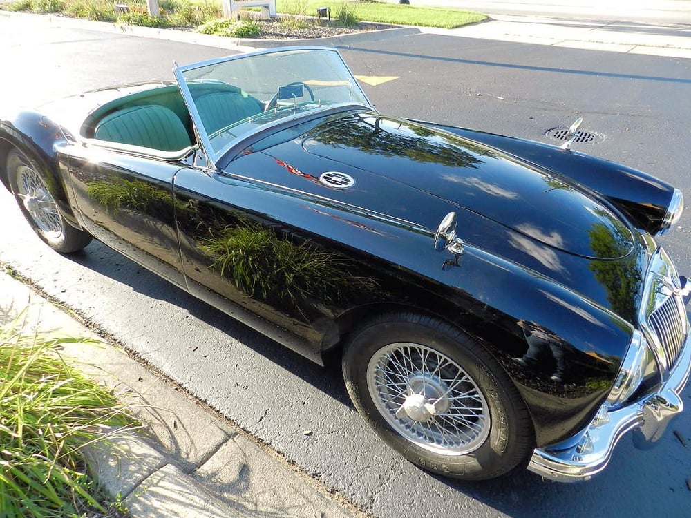 Delivered: gloss black MGA roadster parked top down with chrome wire-spoke wheels and a green interior