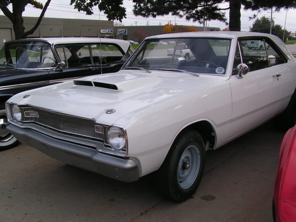 Delivered: white 1968 Dodge Dart coupe with a hood scoop and painted steel wheels at a cruise-in
