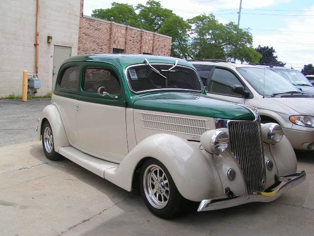 Delivered: two-tone dark green and cream 1936 Ford sedan street rod with alloy wheels parked at the shop
