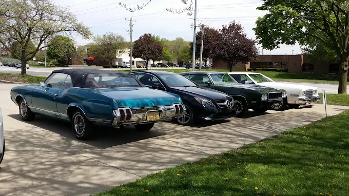 Customer cars lined up outside the shop — a teal 1970 convertible, a Mercedes sedan and classic Fords