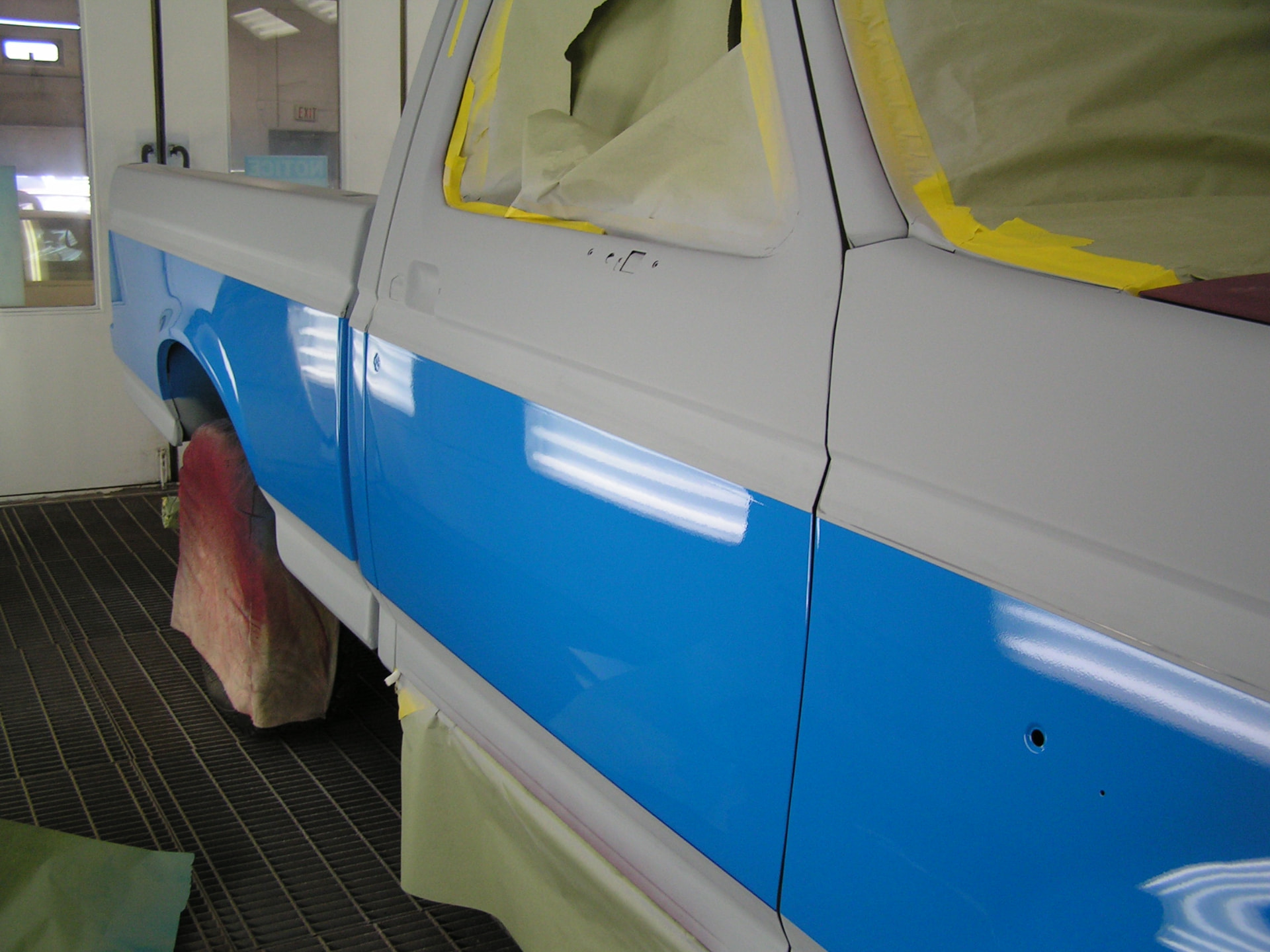 During: Ford F150 cab and bed side in fresh glossy blue paint inside the booth