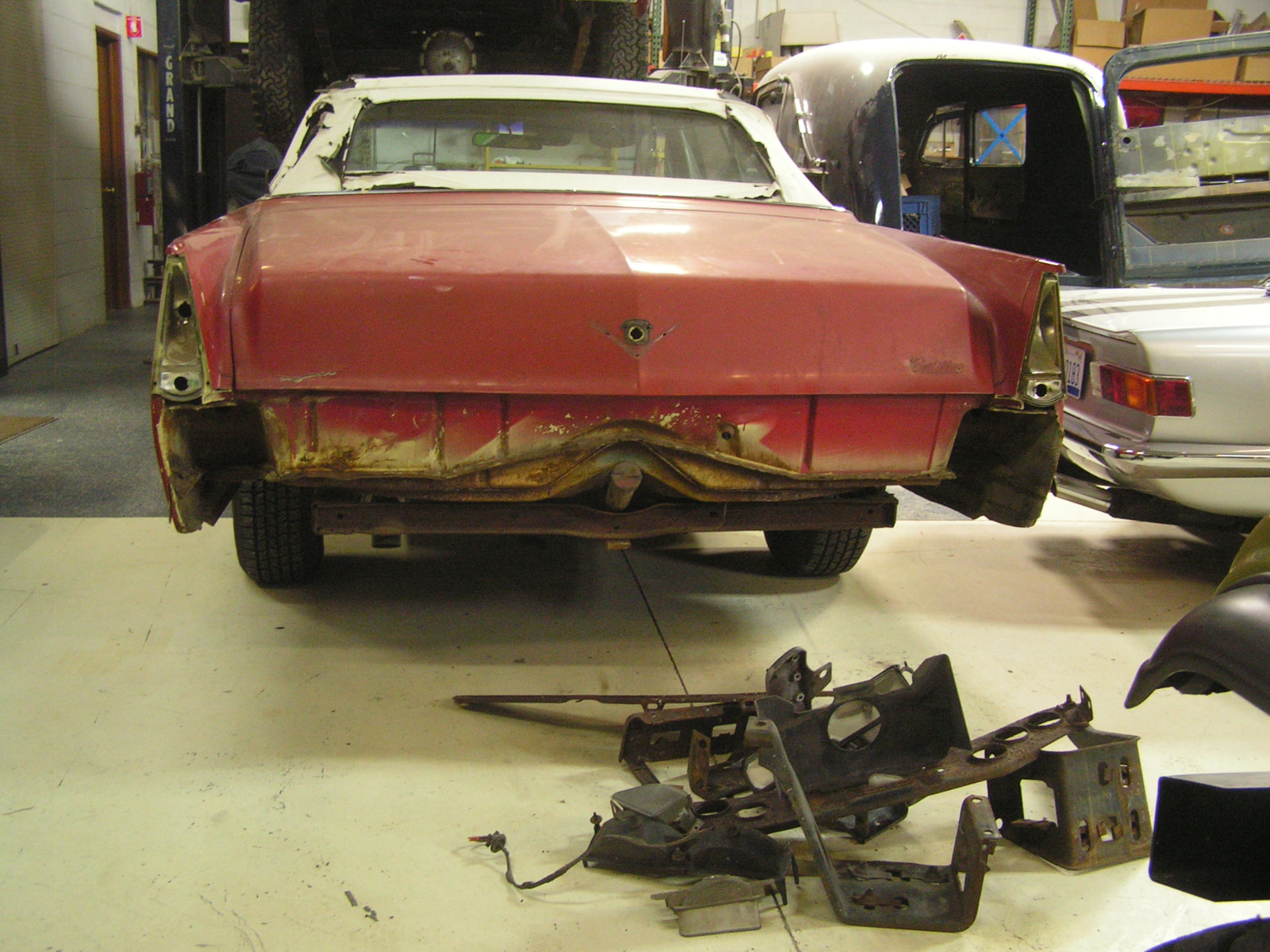 Before: 1969 Cadillac DeVille convertible rear in the shop with bumper, trim and valance removed, damaged lower panel and rusty parts on the floor