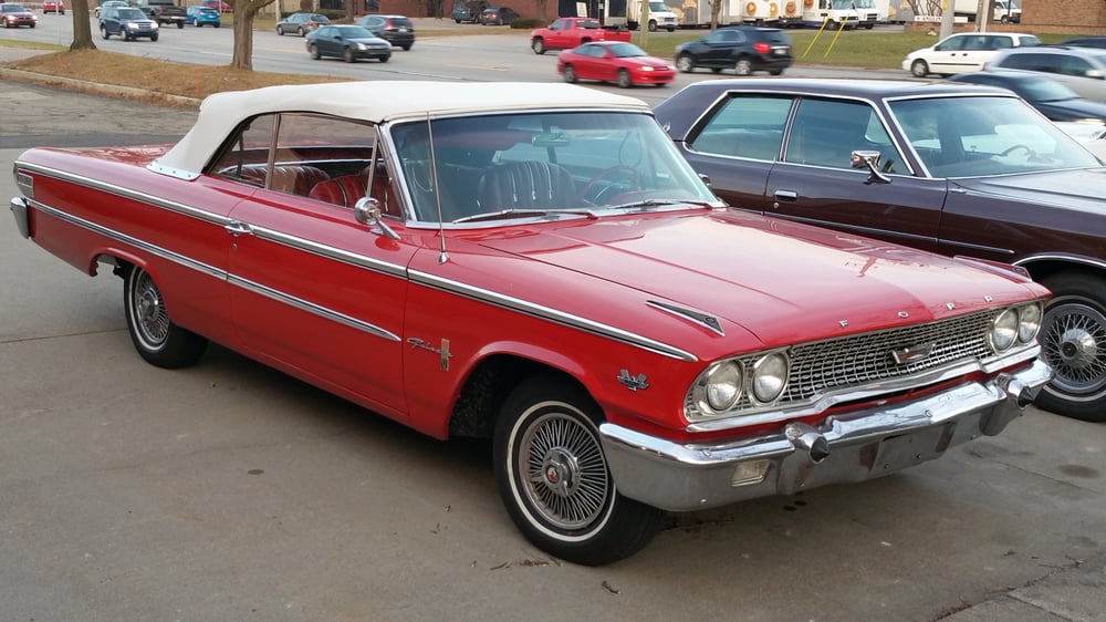 Delivered: bright red 1963 Ford Galaxie 500 convertible with a white soft top parked beside another classic