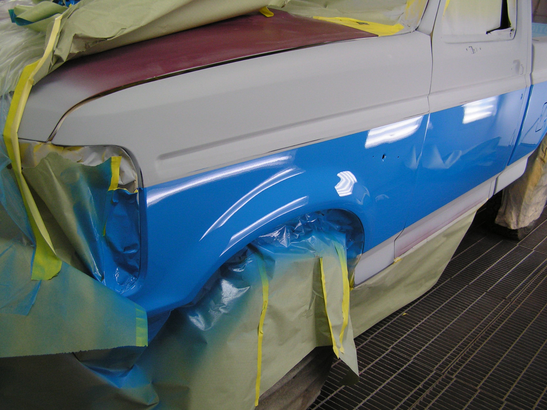 During: 1995 Ford F150 front fender masked off with fresh blue paint laid down in the booth