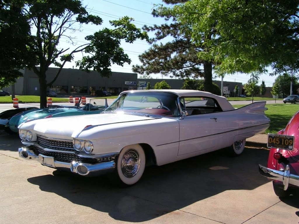 Delivered: white classic Cadillac convertible with tall tailfins, white soft top and red interior, whitewall tires at a car show