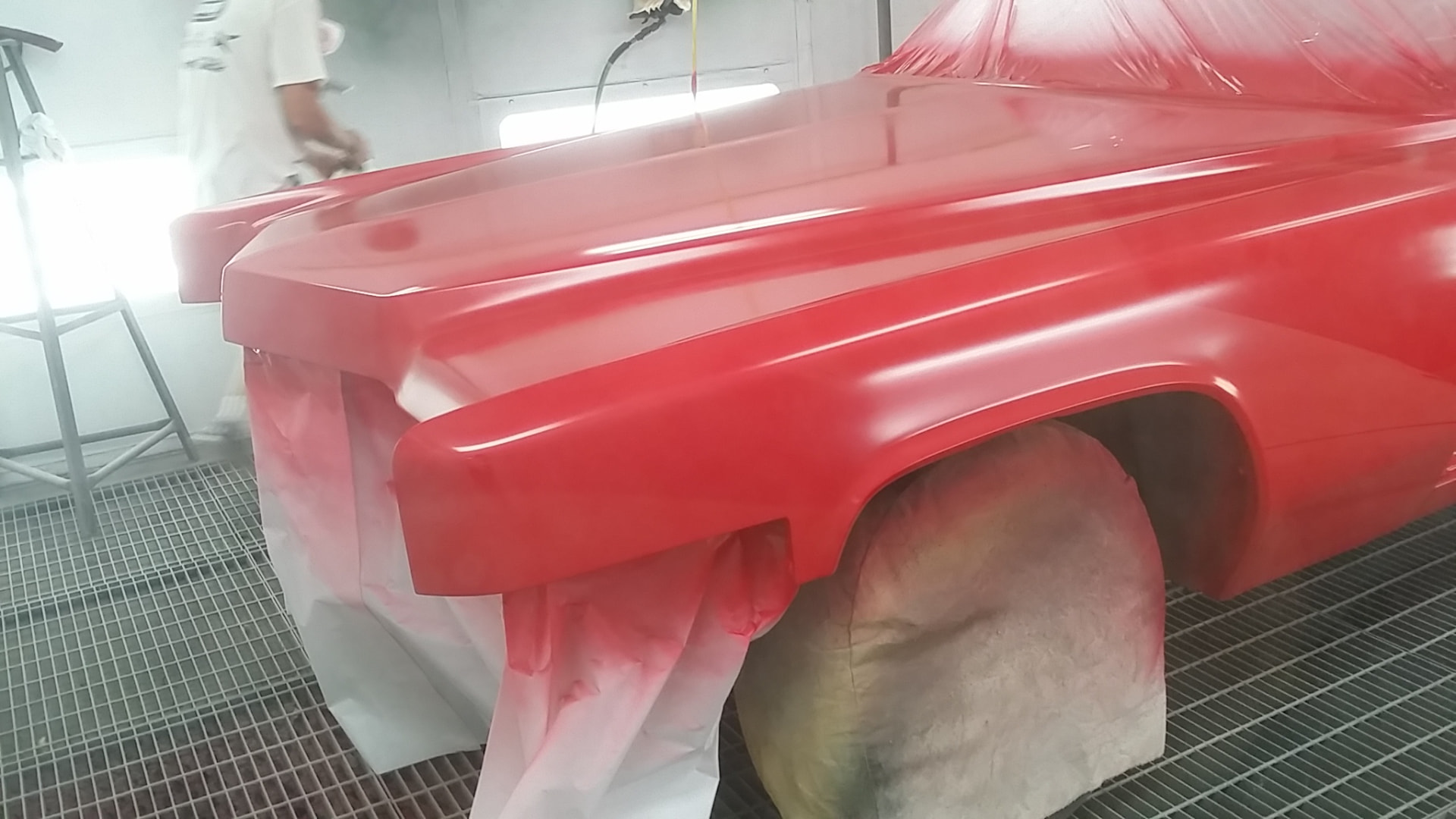 During: fresh red paint sprayed on the Cadillac hood and front fender inside the spray booth